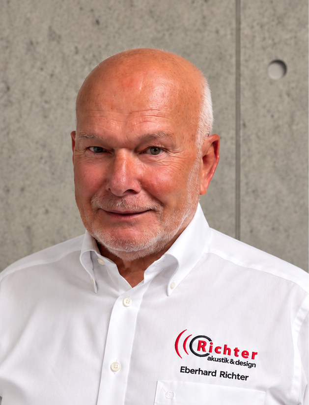 Eberhard Richter smiles confidently in a white shirt, showcasing his expertise in acoustics and design against a gray wall.